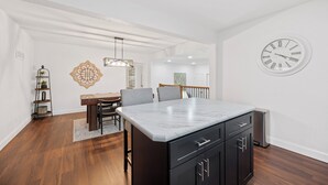 Une cuisine moderne avec un plan de travail en marbre, des meubles de couleur sombre et une horloge au mur.