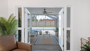 Une porte ouverte donne sur un patio équipé d’un ventilateur de plafond, d’une petite table et de chaises.
