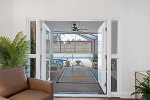 Ein Zimmer mit einer Schiebetür zu einer Außenpatio-Terrasse mit Pool, Sitzgelegenheiten und Deckenventilator.