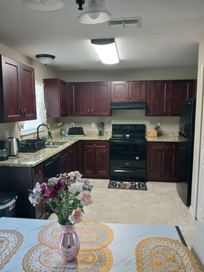 A kitchen with dark wooden cabinets, a black stove, a refrigerator, and a sink. - Charming 3-bedroom house with AC, WiFi in awesome Ocala (Ocala)
