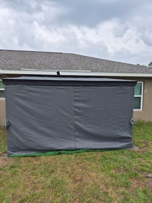 A grey, enclosed structure with a roof, situated in a grassy area with a building in the background. - Charming 3-bedroom house with AC, WiFi in awesome Ocala (Ocala)