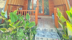 A wooden cabin with a sloped roof, a porch with a railing, and a stone-tiled entrance. - Kintamani Angel (Kintamani)
