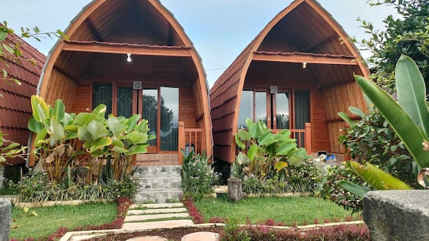 Two wooden cabins with pitched roofs, a stone staircase leading to the entrance, and a well-maintained garden with various plants and a stone pathway. - Kintamani Angel (Kintamani)