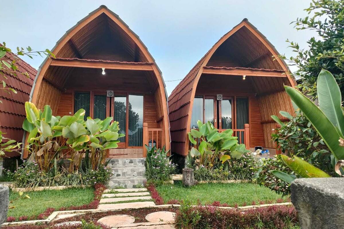 Two wooden cabins with pitched roofs, a stone staircase leading to the entrance, and a well-maintained garden with various plants and a stone pathway.