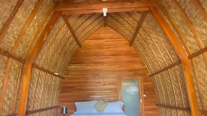 A cozy attic bedroom with a wooden ceiling and walls, a bed with a blue bedspread, and a small bedside table. - Kintamani Angel (Kintamani)