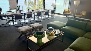 A modern room with a large window overlooking a lake, a dining area with a table and chairs, and a green sofa. - Peats Bite  (Berowra Waters)