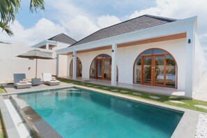 Una casa moderna con piscina, mobiliario exterior y ventanas amplias.