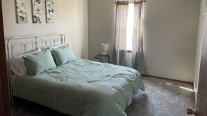 Un dormitorio con cama, mesita de noche, lámpara y ventana con cortinas.