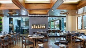 A restaurant with wooden ceiling beams, a central fireplace, and a view of the outdoors through large windows. - Resort in Las Vegas with NO RESORT FEES & FREE VALET SERVICE! (Las Vegas)
