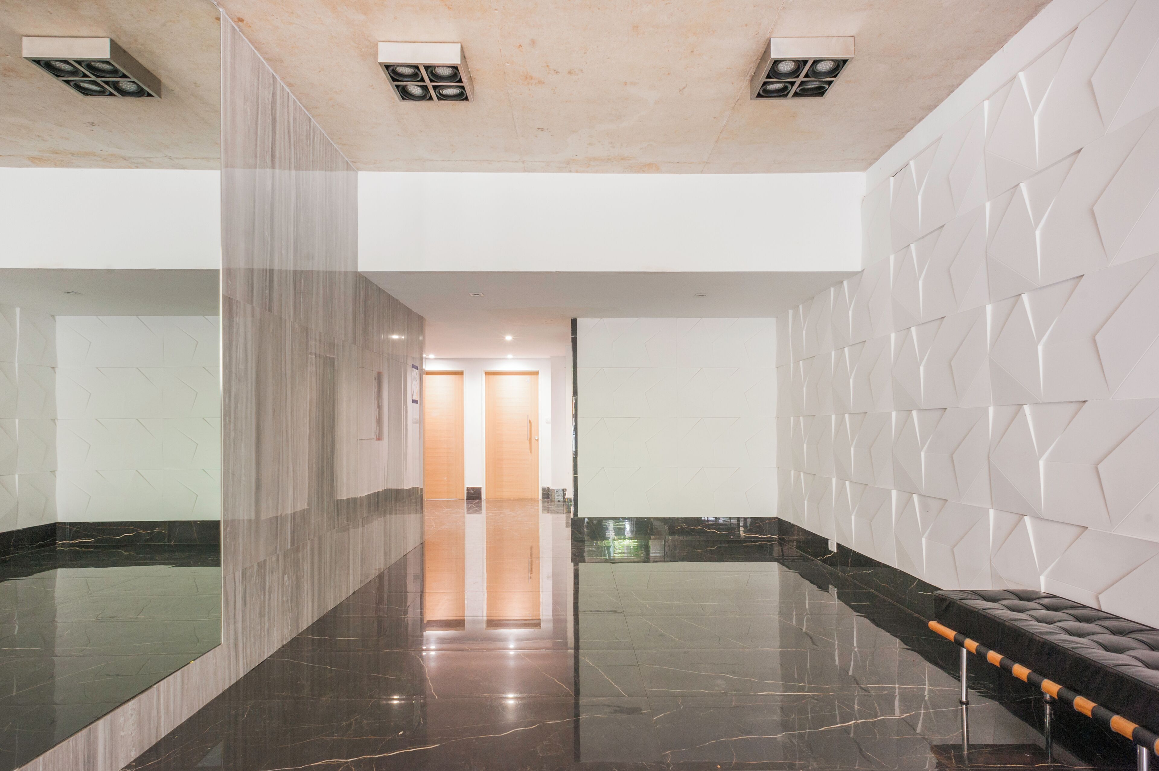 Una hall moderna con pavimento in marmo, una panca in pelle nera e un design geometrico per le pareti.