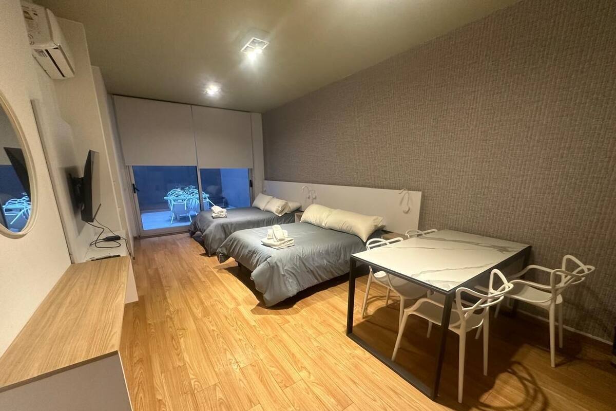 A modern bedroom with two beds, a dining table, and a TV.