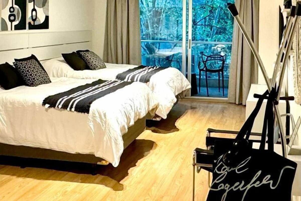 A bedroom with two beds, a balcony with a chair, and a camera on a tripod.