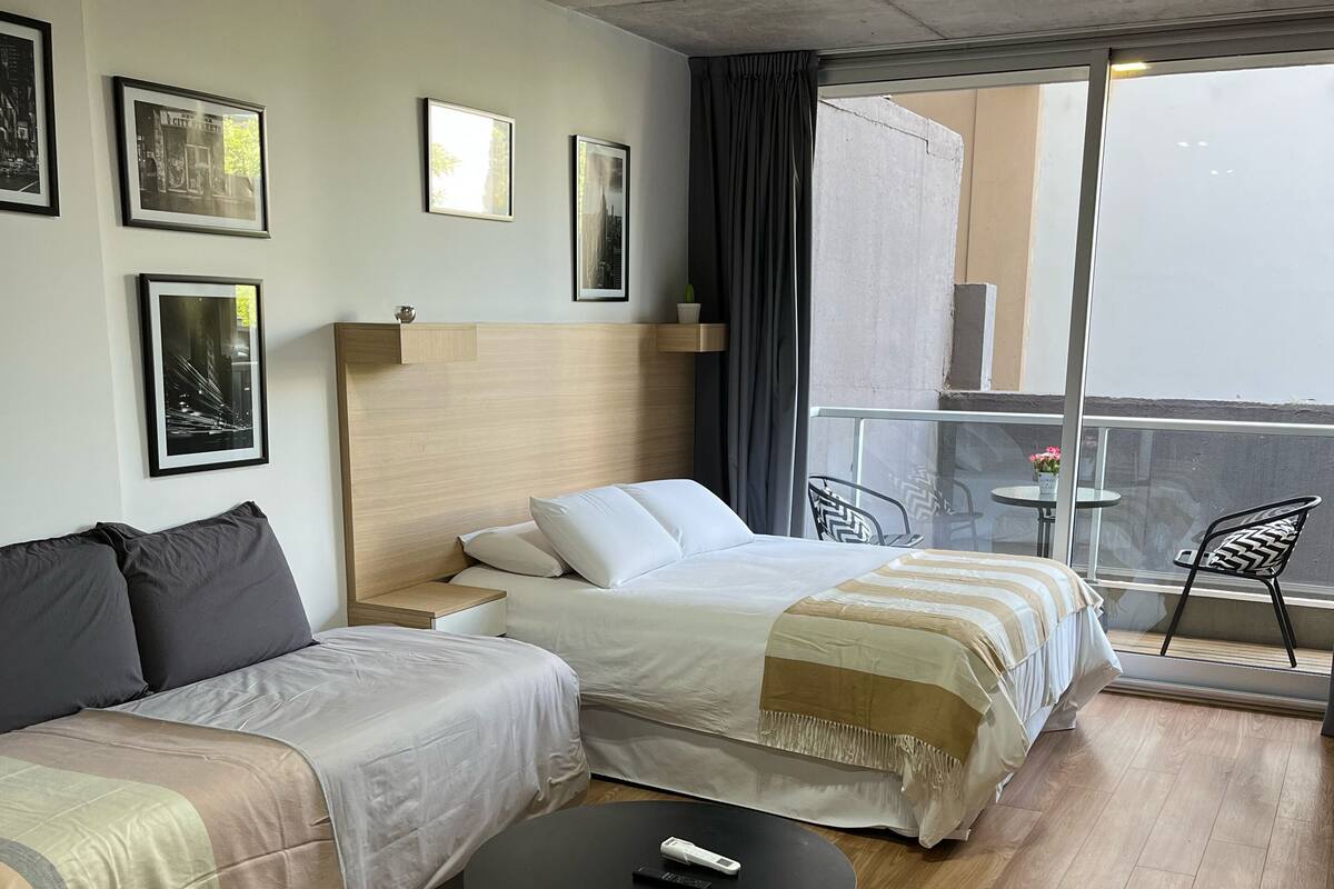 A hotel room with two beds, a sofa, a small table, and a balcony with a chair.