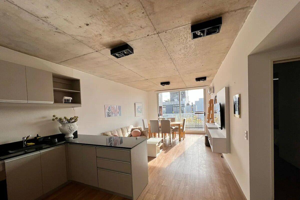 A modern kitchen with a central island, wooden flooring, and a dining area with chairs and a table.
