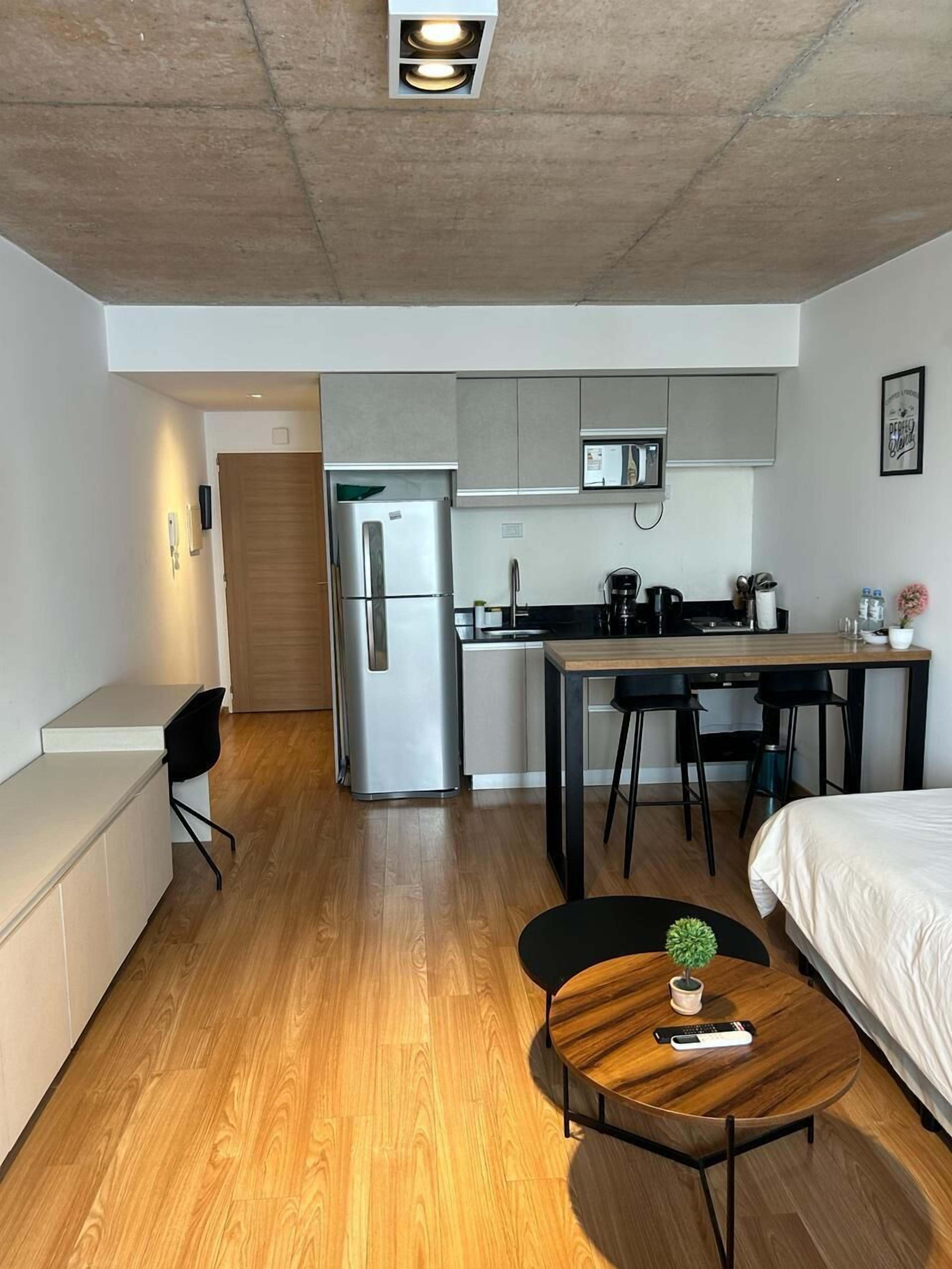 Ein kleines Hotelzimmer mit Küchenzeile, Essbereich und einer Sitzecke mit rundem Tisch und Topfpflanze.
