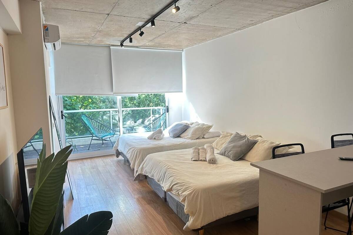 A modern bedroom with two beds, a desk, and a balcony with chairs.