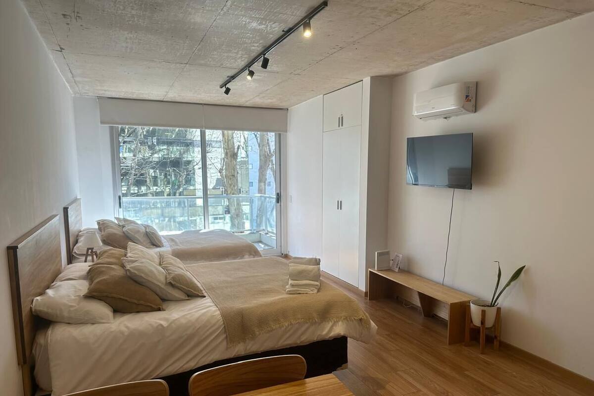 A modern bedroom with a large bed, a TV mounted on the wall, and a window providing a view of the outside.