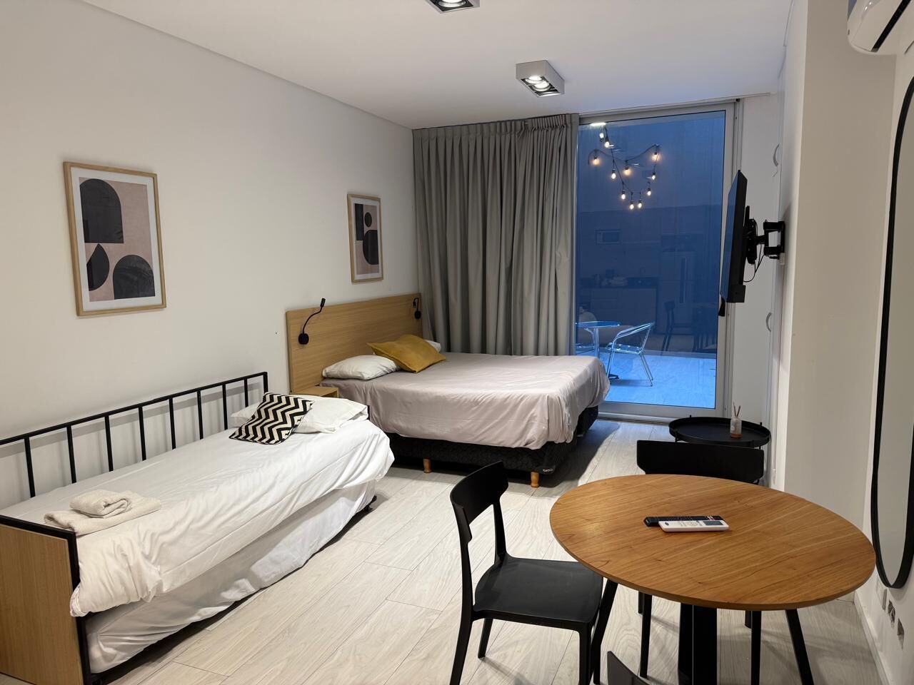 Una habitación de hotel con dos camas individuales, un cabecero de madera, una mesita redonda pequeña y una silla.