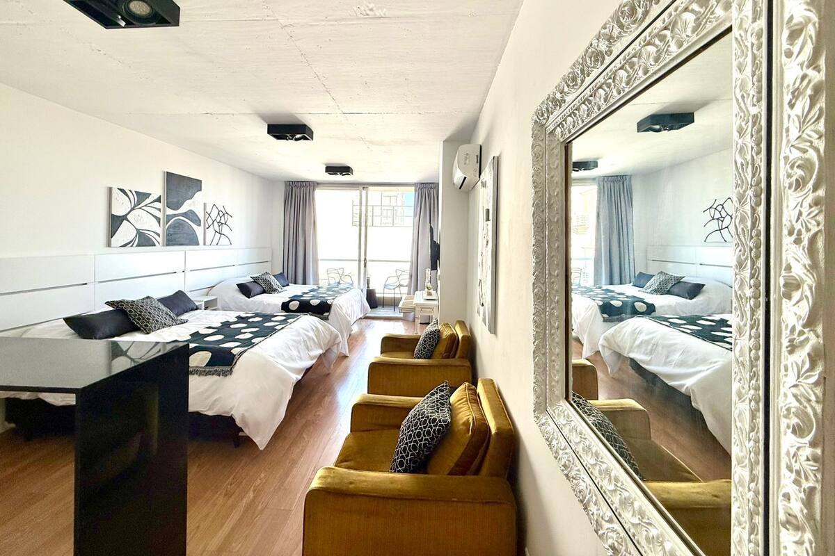 A hotel room with a large bed, a sofa, a dining table, and a mirror.
