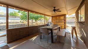 A covered patio with a table and chairs, a ceiling fan, and a view of the outside. - The Latham Abode | Spa | Firepit | Game Room | NEW (Joshua Tree)
