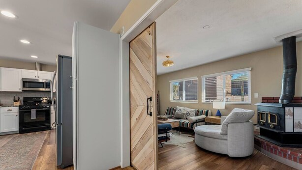 A modern kitchen with white cabinets, a black refrigerator, and a stove. There is a wooden door leading to a living area with a sofa, a table, and a fireplace. - The Latham Abode | Spa | Firepit | Game Room | NEW (Joshua Tree)