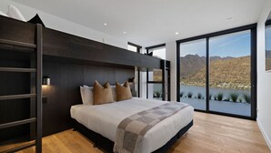 A modern bedroom with a large bed, a built-in ladder, and a scenic view of a lake and mountains. - The Bunker Charlie A-2 Bedroom (Queenstown)