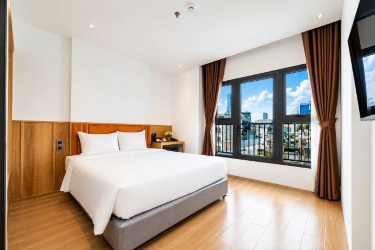 A hotel room with a large bed, wooden paneling, a nightstand, a TV, and a window with curtains.