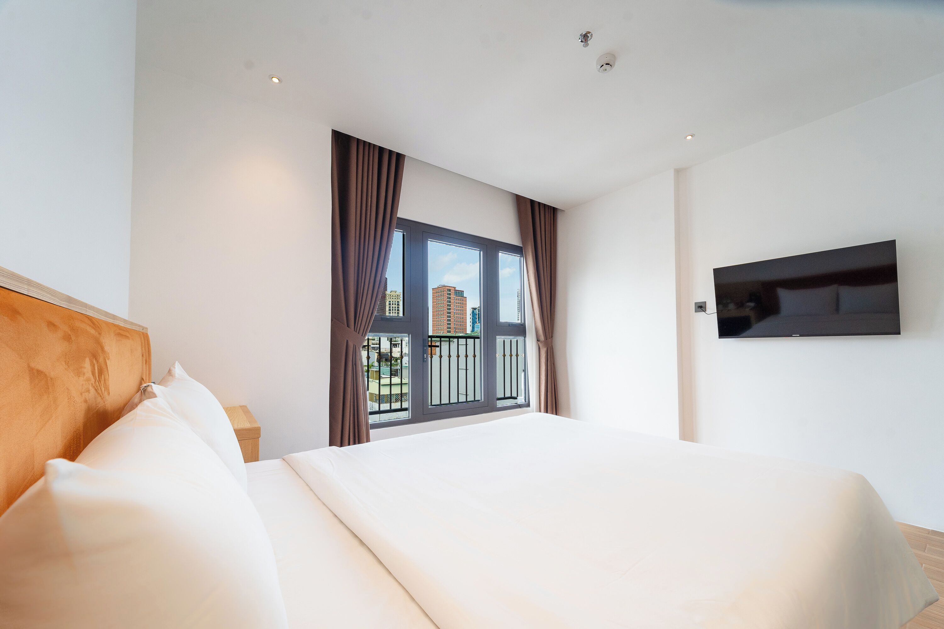A modern hotel room with a large bed, a TV mounted on the wall, and a balcony with a view of the city.