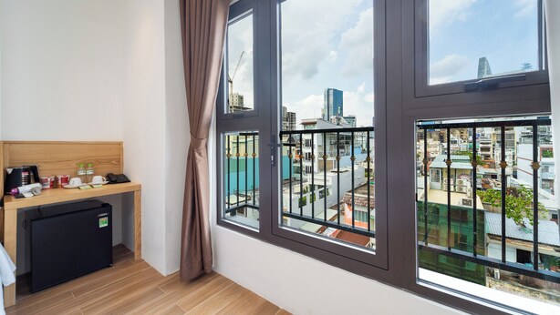 Una habitación con un escritorio de madera, un refrigerador pequeño y un ventanal con vistas a edificios de la ciudad.