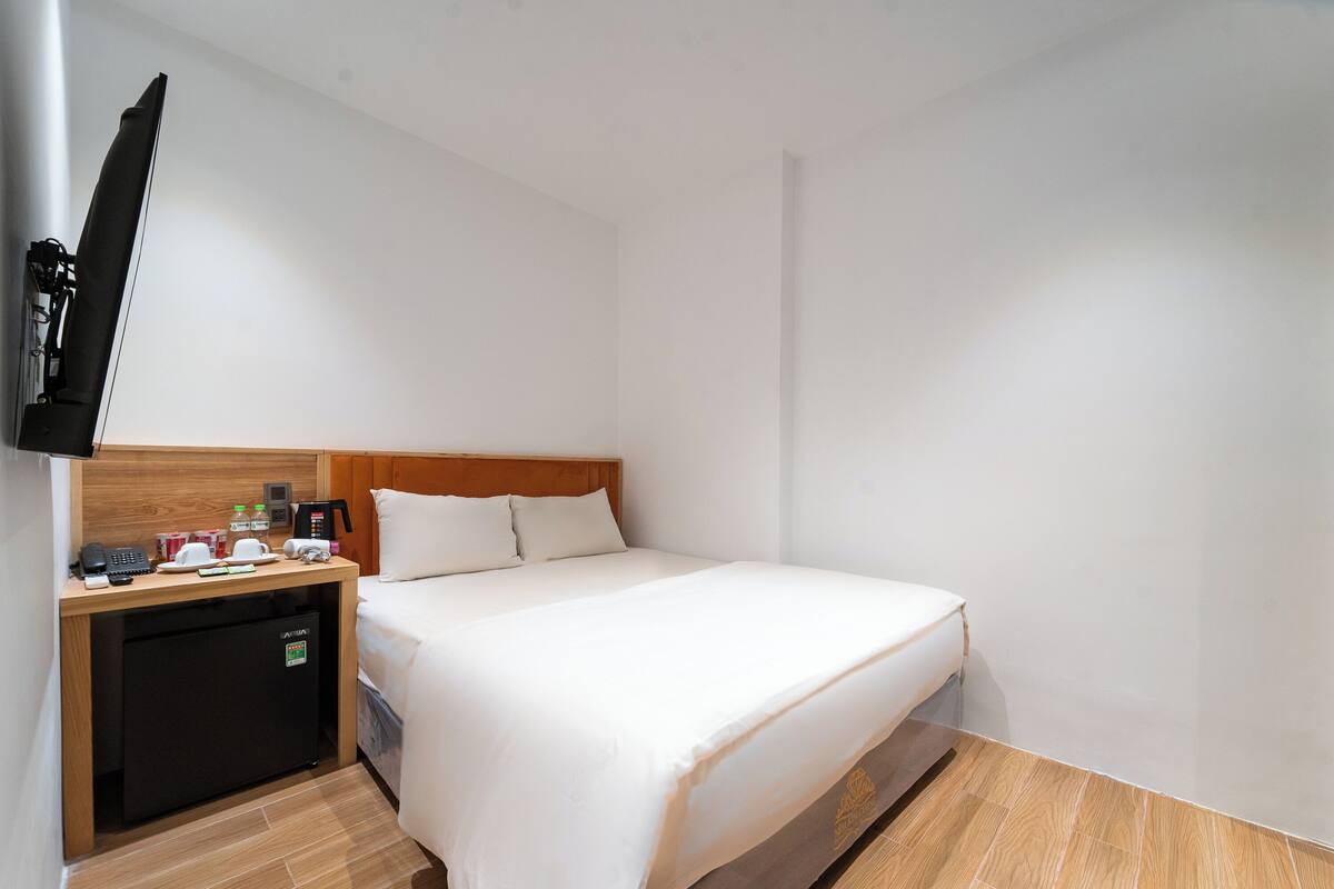 Habitación de hotel con cama, un escritorio pequeño con cafetera, refrigerador y televisor de pantalla plana montado en la pared.