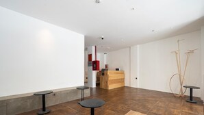 Un interior moderno con una mesa de recepción, tres mesas pequeñas y piso de madera.
