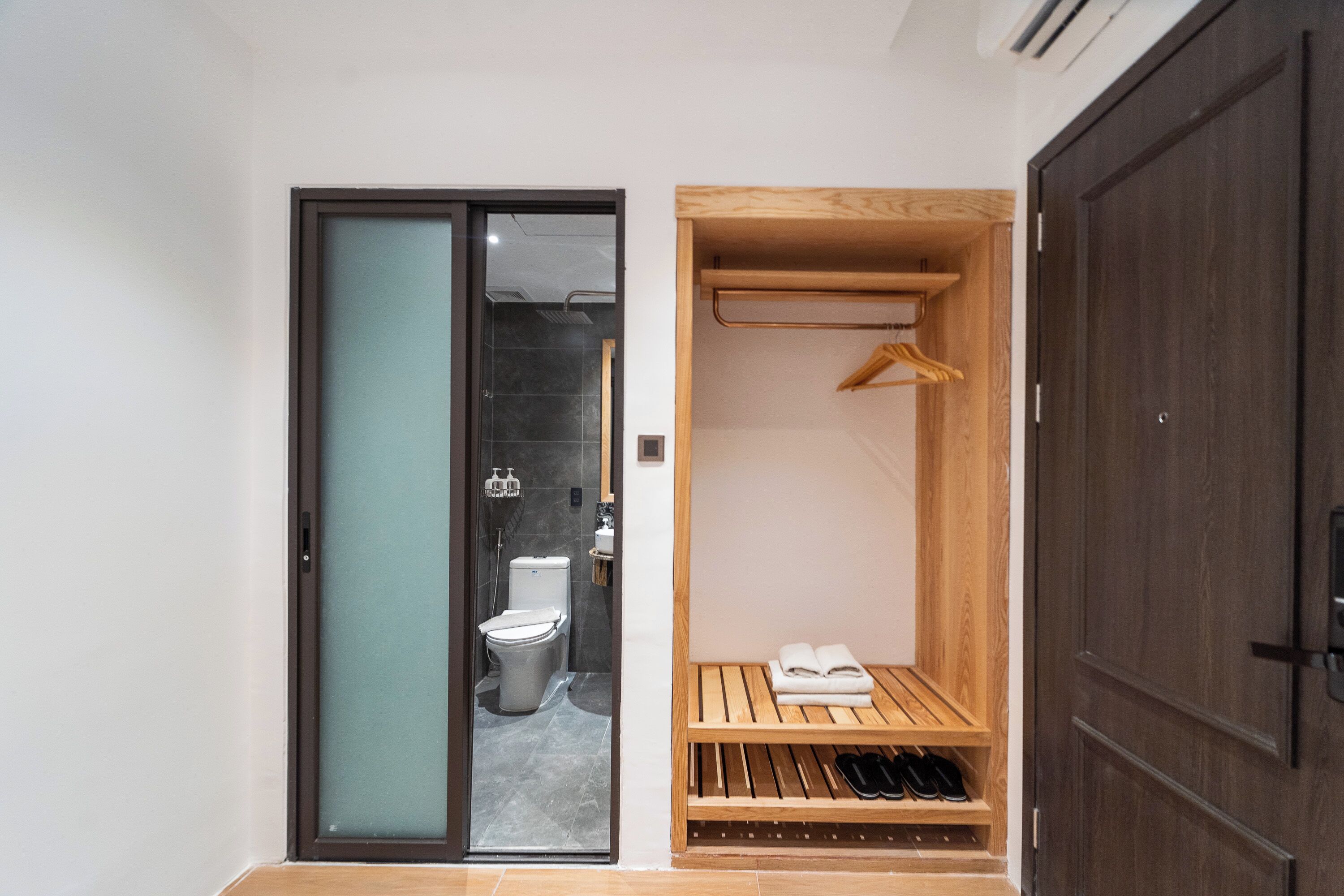 A modern bathroom with a glass door, a wooden bench, and a towel rack.
