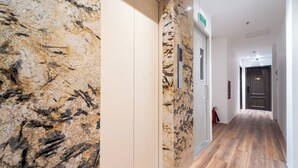 Un pasillo con pared de mármol, suelo de madera y una puerta con señal de salida de emergencia.