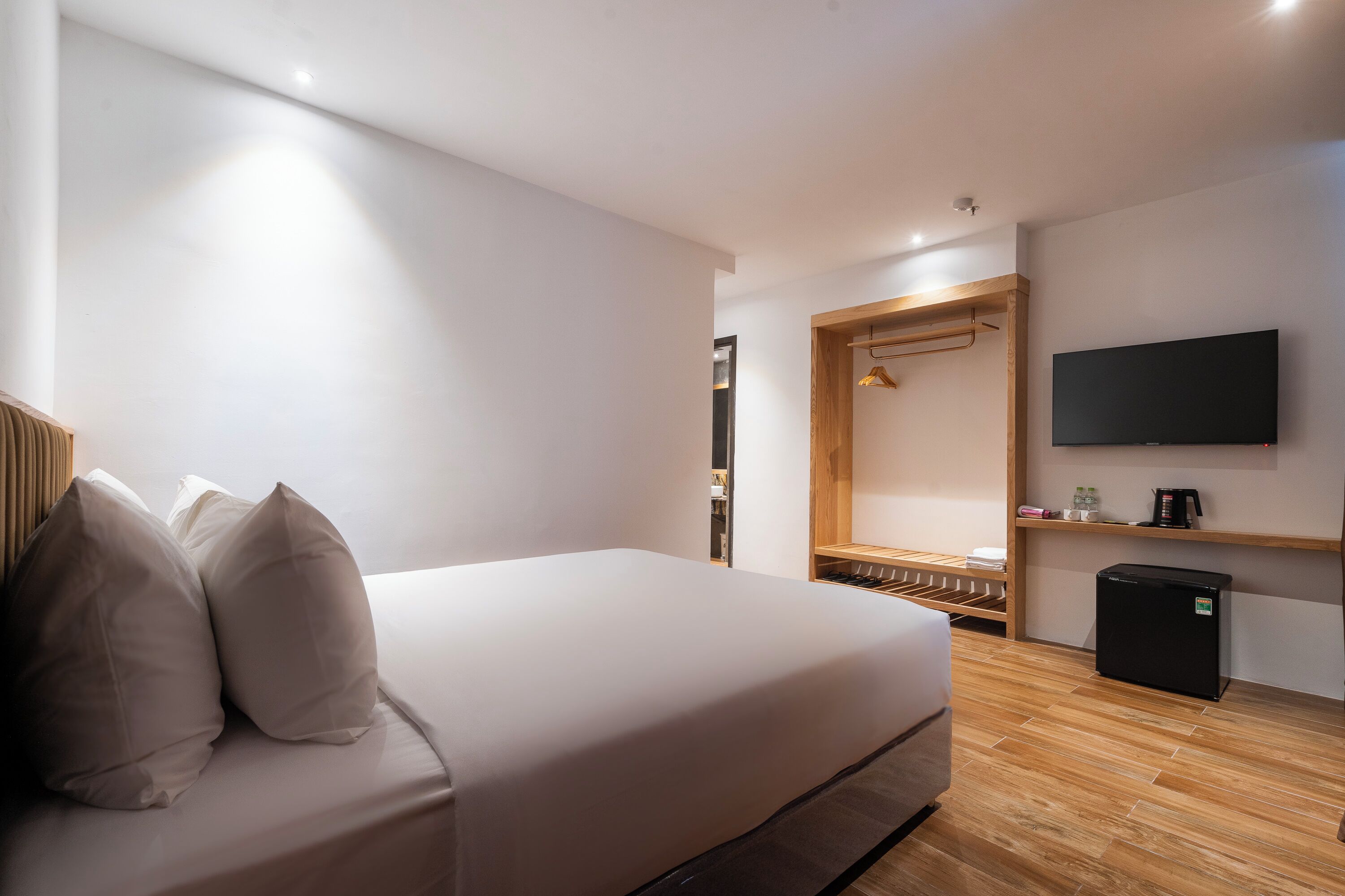 Habitación de hotel moderna con cama, televisor, refrigerador pequeño y estante de madera con espejo y perchero.