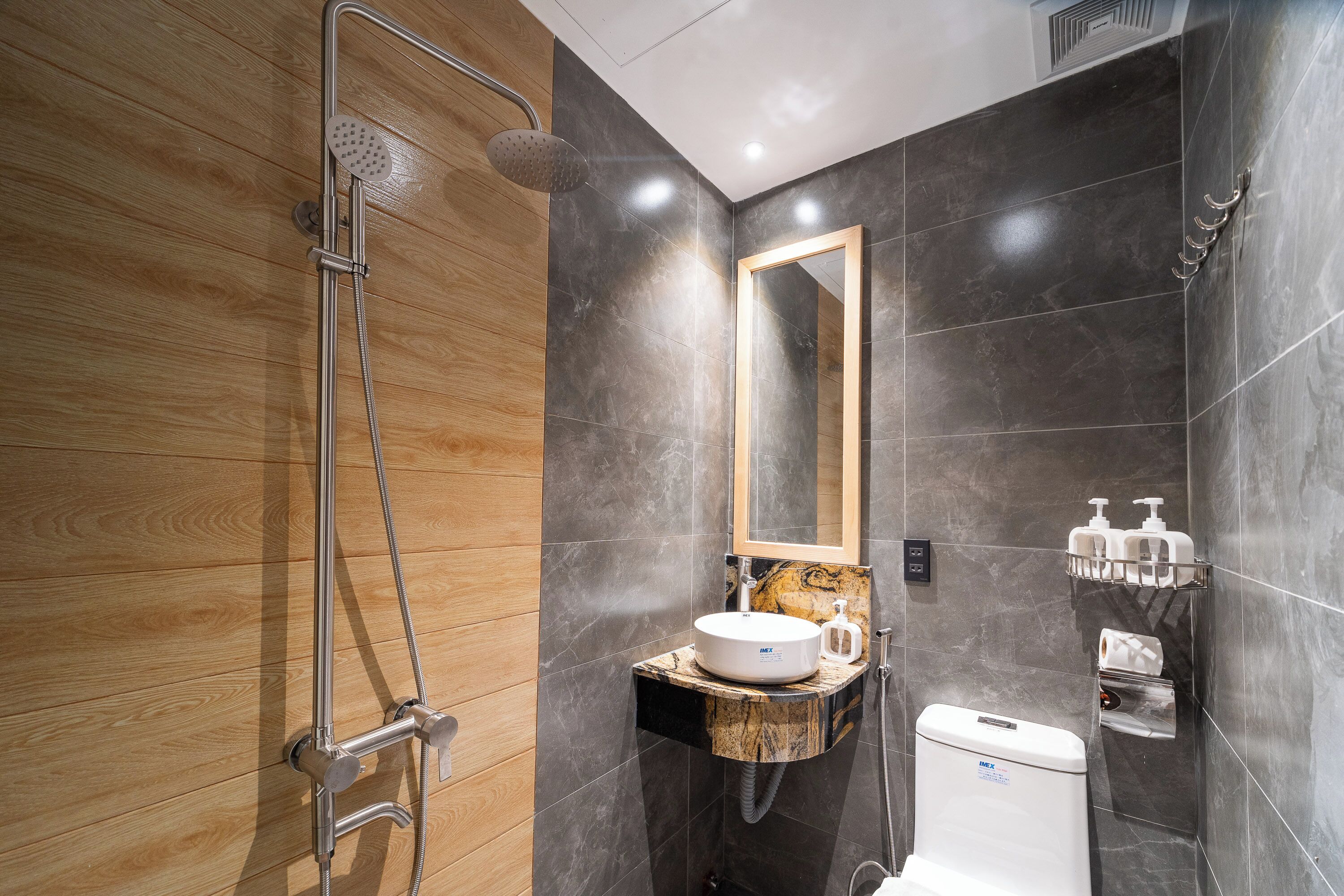 Een moderne badkamer met een houten vloer, een douchegedeelte betegeld met marmer, een wastafel met een marmeren blad en een spiegel boven de wastafel.
