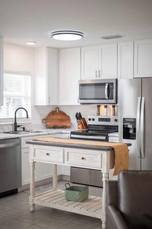 A modern kitchen with white cabinetry, a wooden cutting board, a stainless steel refrigerator, and a built-in oven.