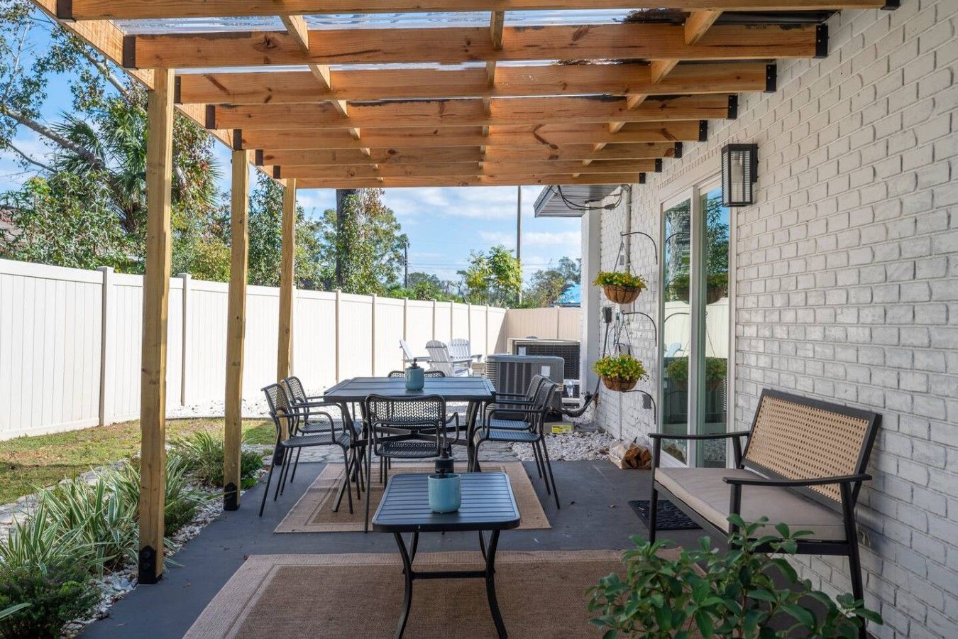 An outdoor patio with a wooden pergola, a table with chairs, and a grill.