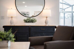 Une pièce avec une commode en bois foncé, deux lampes fixées au mur, un miroir et une plante en pot.