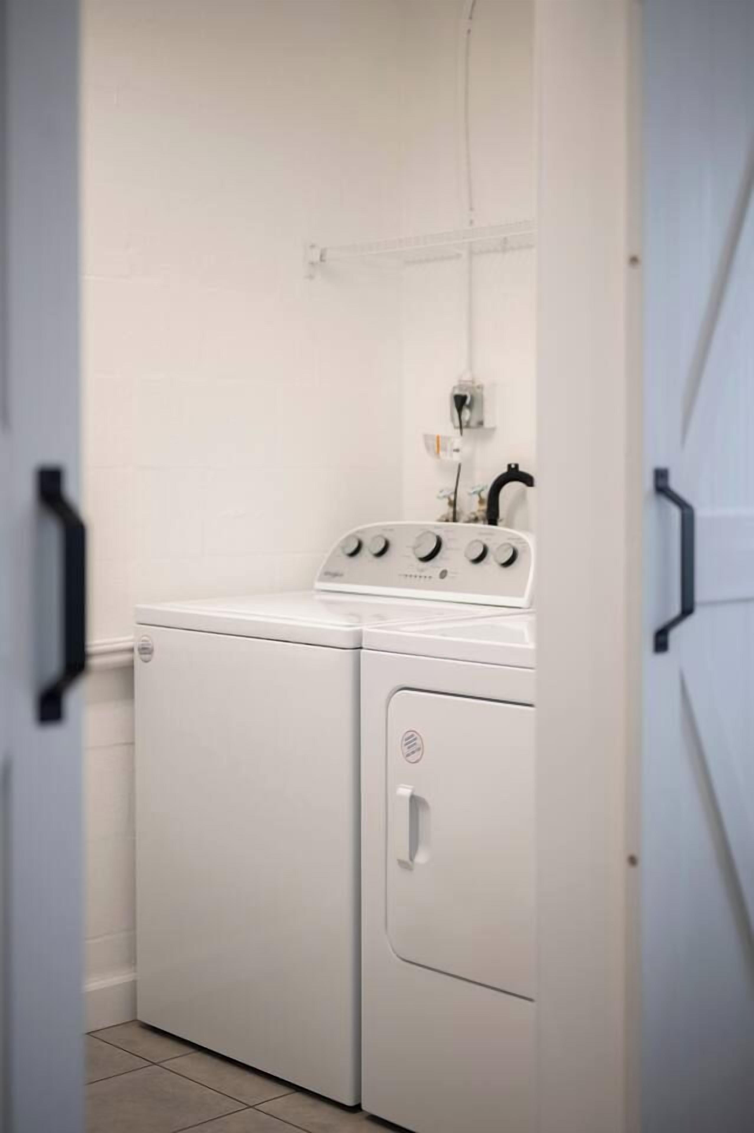 A laundry room with a front-loading washer and dryer, a control panel, and a power outlet on the wall.