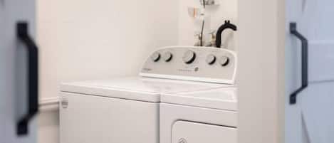 A laundry room with a front-loading washer and dryer, a control panel, and a power outlet on the wall.