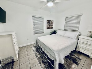 A bedroom with a bed, a dresser, a radiator, and two windows with blinds.