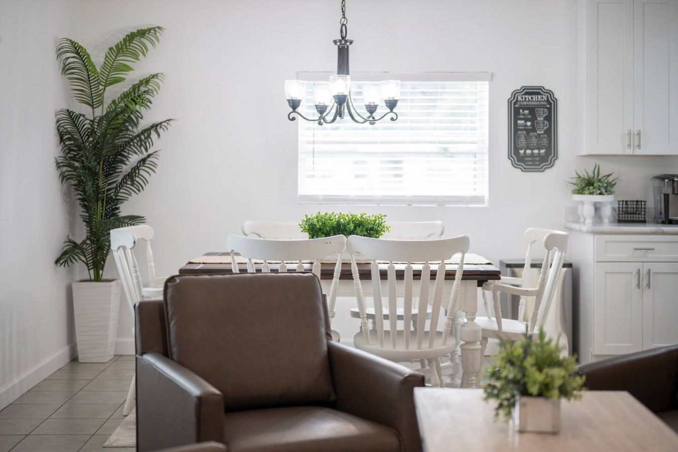 A dining area with a chandelier, white chairs, a table, and a potted plant.