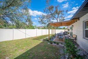 Un jardin avec un patio couvert, une clôture blanche et une maison en briques.