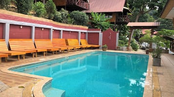 Una piscina con tumbonas de madera y un suelo de baldosas.