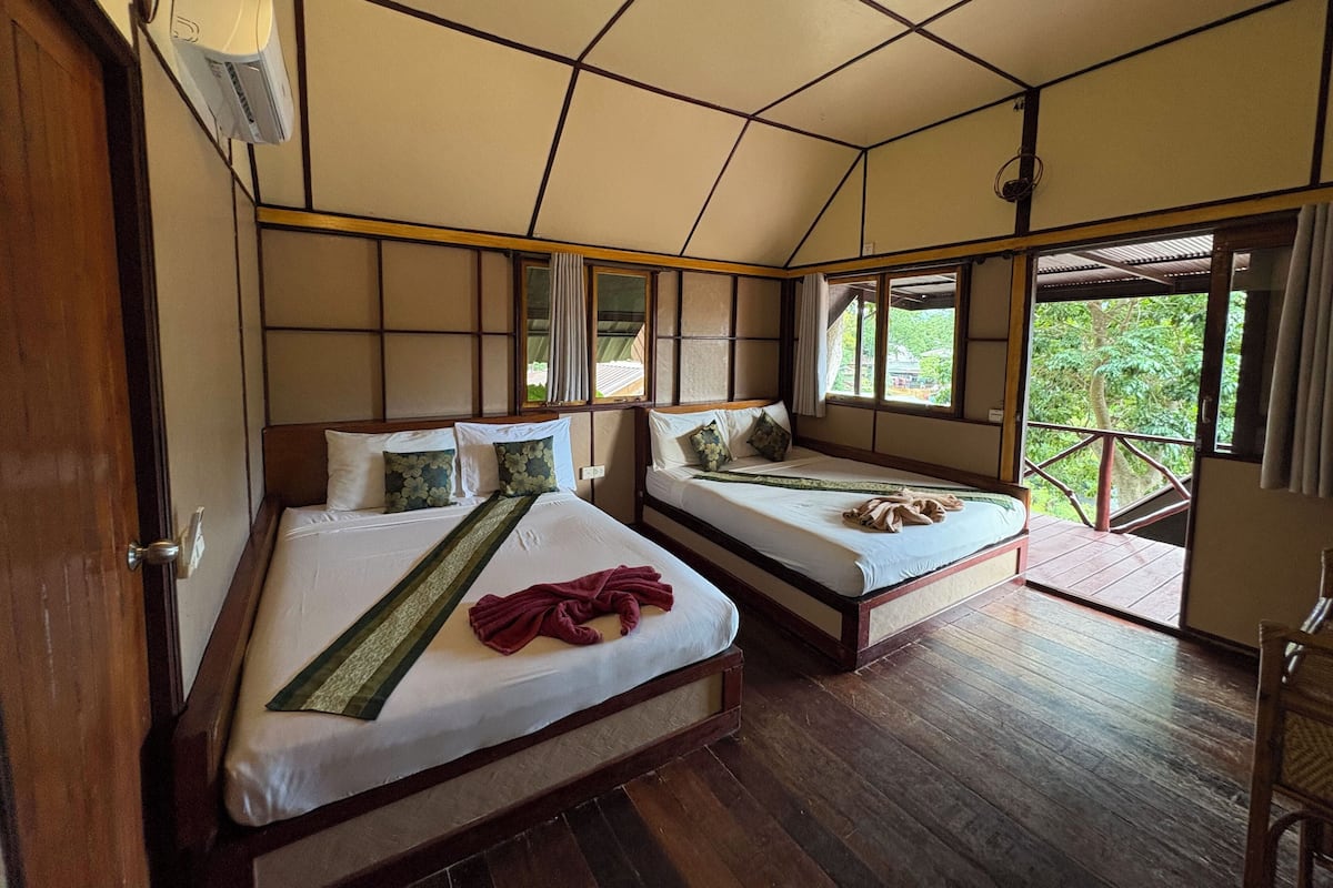 Une chambre avec deux lits, un plancher en bois, un ventilateur de plafond et une fenêtre donnant sur un paysage verdoyant.