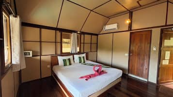 Quarto de hotel com uma cama grande, piso de madeira, janela com cortinas, ar condicionado e porta de madeira.