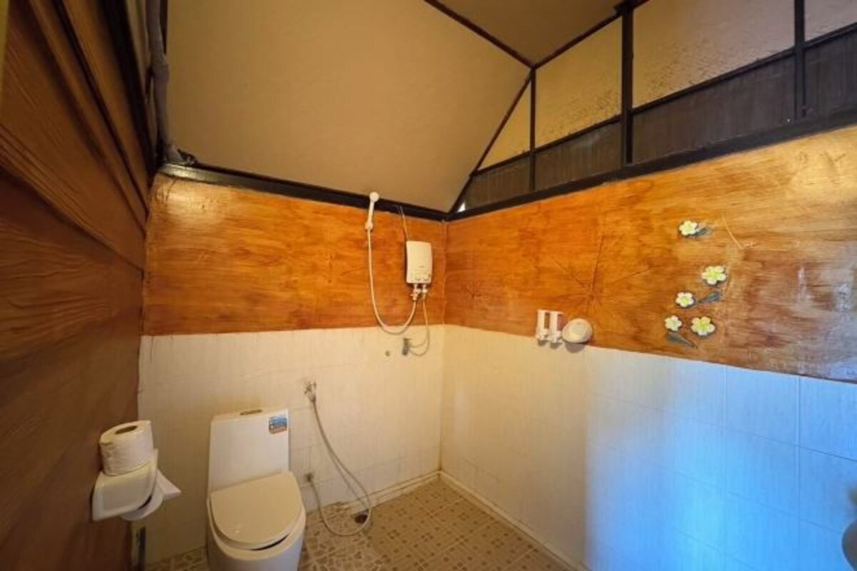 A bathroom with a wooden accent wall, a toilet, a shower, and a towel rack.