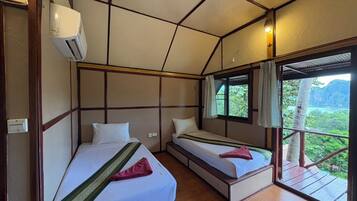 A room with two beds, a window with curtains, and an air conditioning unit.
