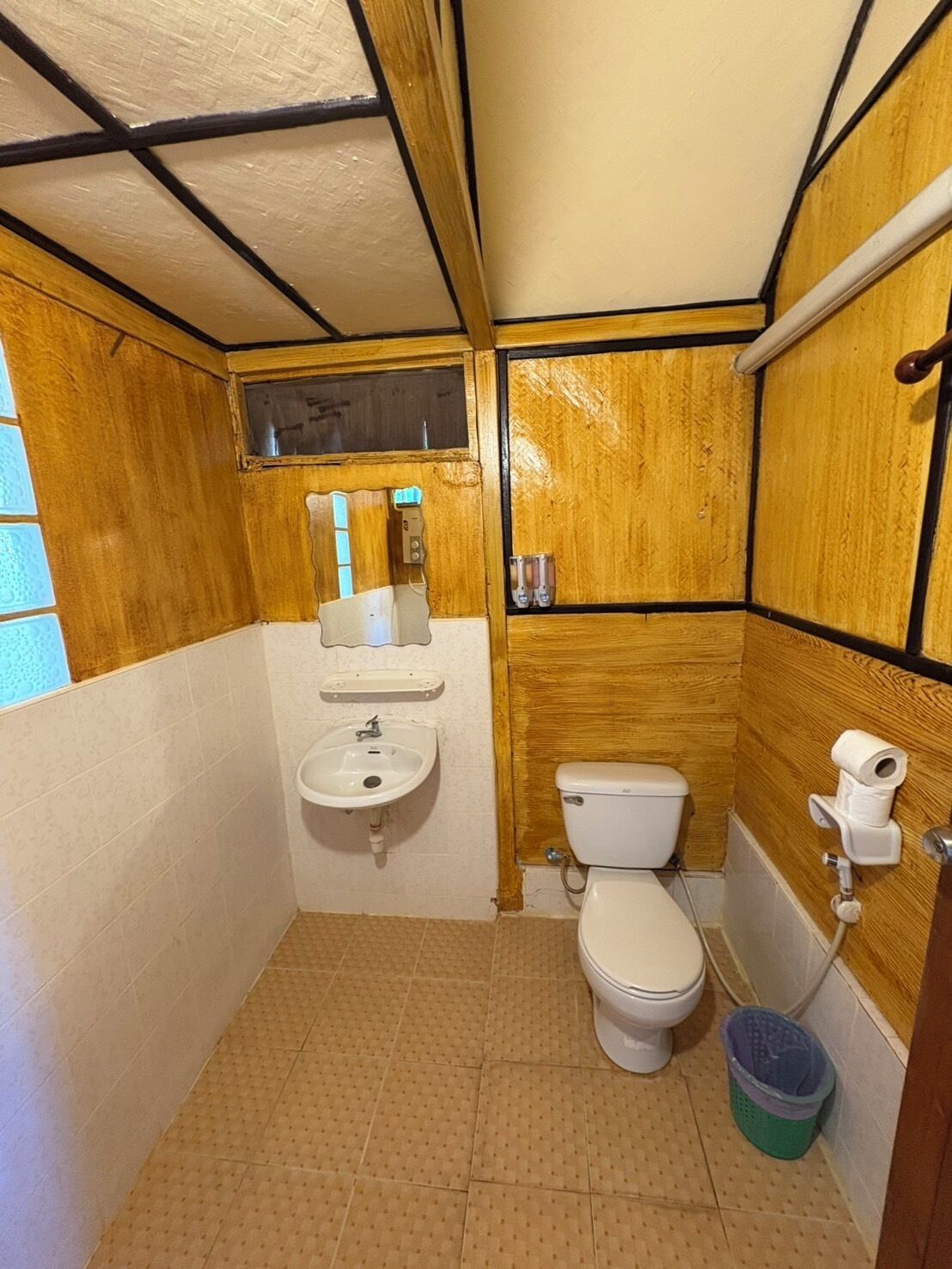 A compact bathroom with a wooden interior, a white sink, a toilet, and a small trash bin.
