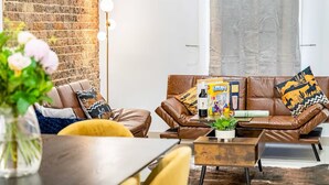 Una sala moderna con pared de ladrillo, sofás de cuero, una mesa de centro y una lámpara de pie.